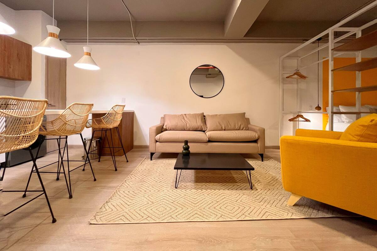 Een moderne woonkamer met een beige bank, een gele fauteuil, rieten stoelen en een salontafel.