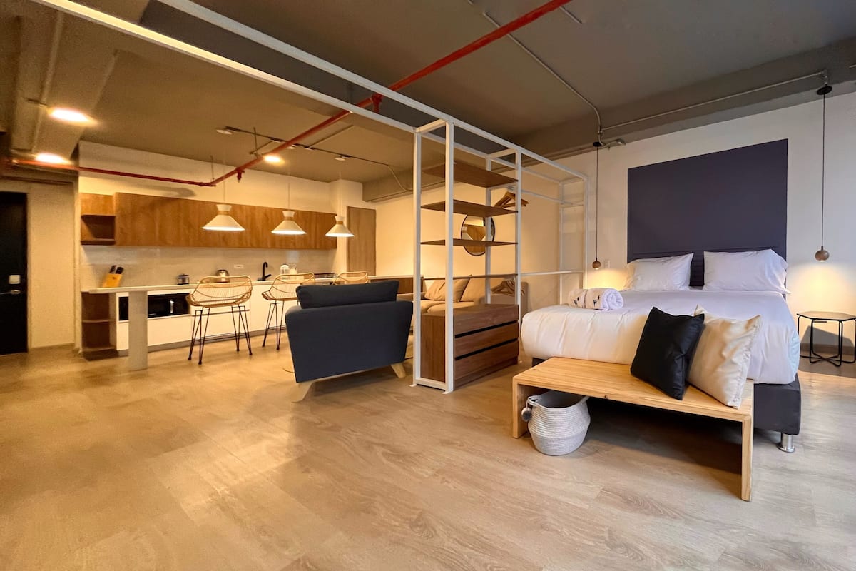 Een moderne hotelkamer met een groot bed, een bureau, een stoel, een bank en een keuken in de achtergrond.