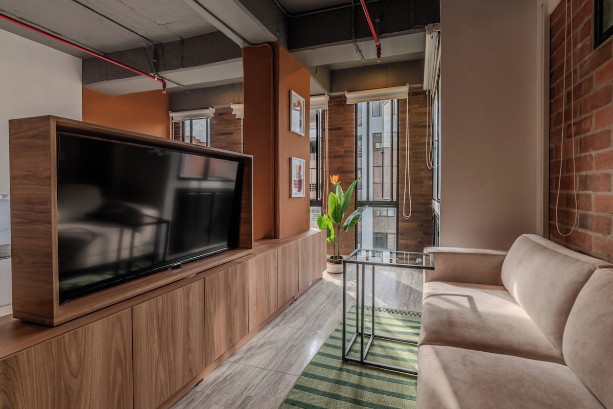 Een moderne woonkamer met een flatscreen televisie, houten kasten, een glazen salontafel en een beige bank.