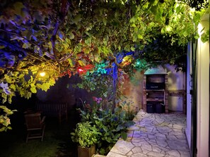 A stone-tiled patio with a wooden chair and a small table, surrounded by lush greenery and vines. - Biarritz - Maison de Ville Avec Jardin, les Plages à Moins de 15 Minutes à Pied (Biarritz)
