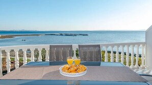Ein Balkon mit Frühstückstisch, mit Blick auf ruhiges Meer und entfernte Küste.