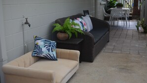 A covered outdoor seating area with a beige sofa and a dark brown sofa, both with cushions. There is a potted plant on the dark brown sofa. - Alice Street 1, Unit 1, Currimundi (Currimundi)
