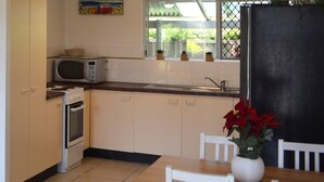 A compact kitchen with a microwave, oven, and sink. There is a window with a view of greenery outside. - Alice Street 1, Unit 1, Currimundi (Currimundi)