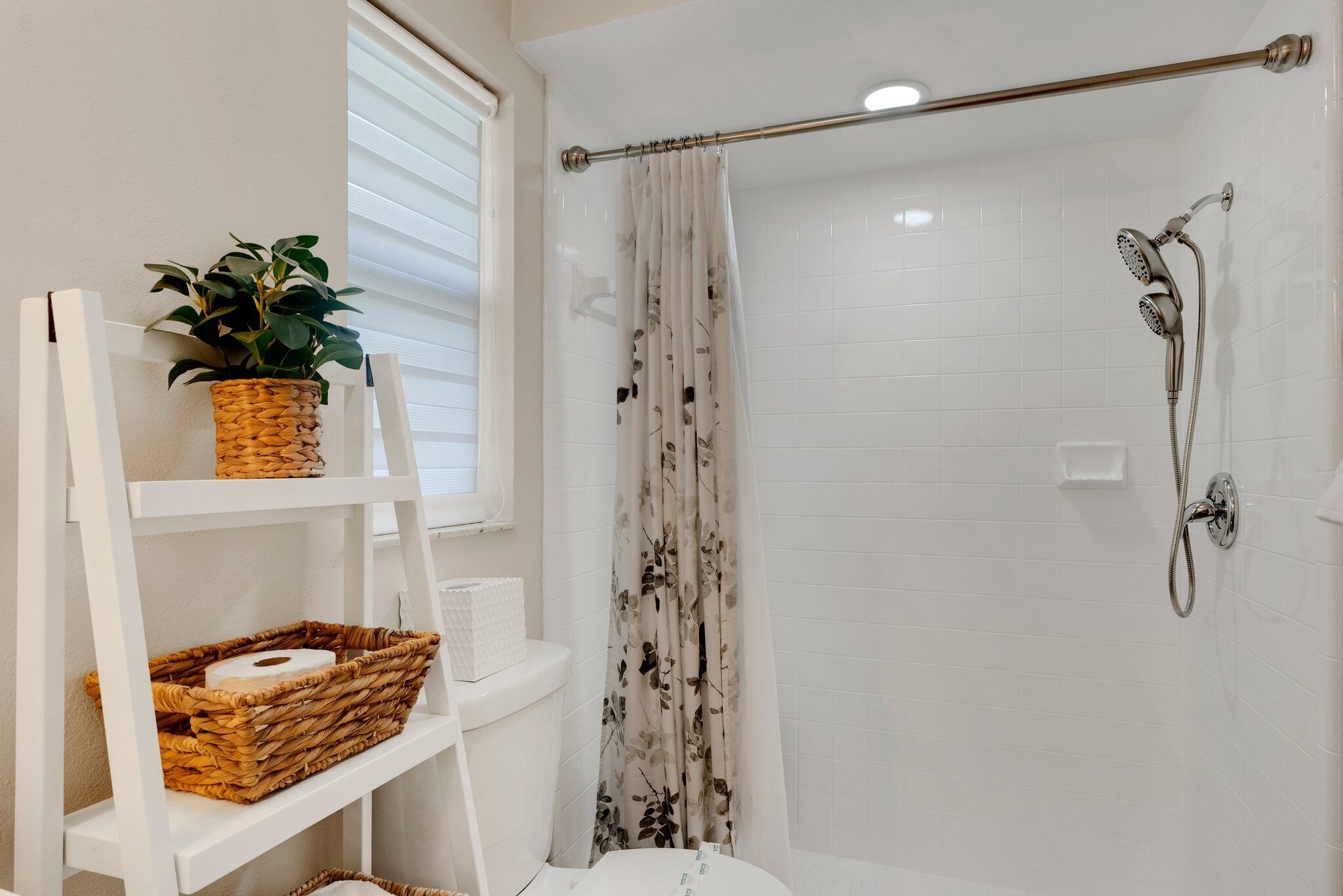 A bathroom with a shower, a white shelf with a plant and a basket, and a toilet.