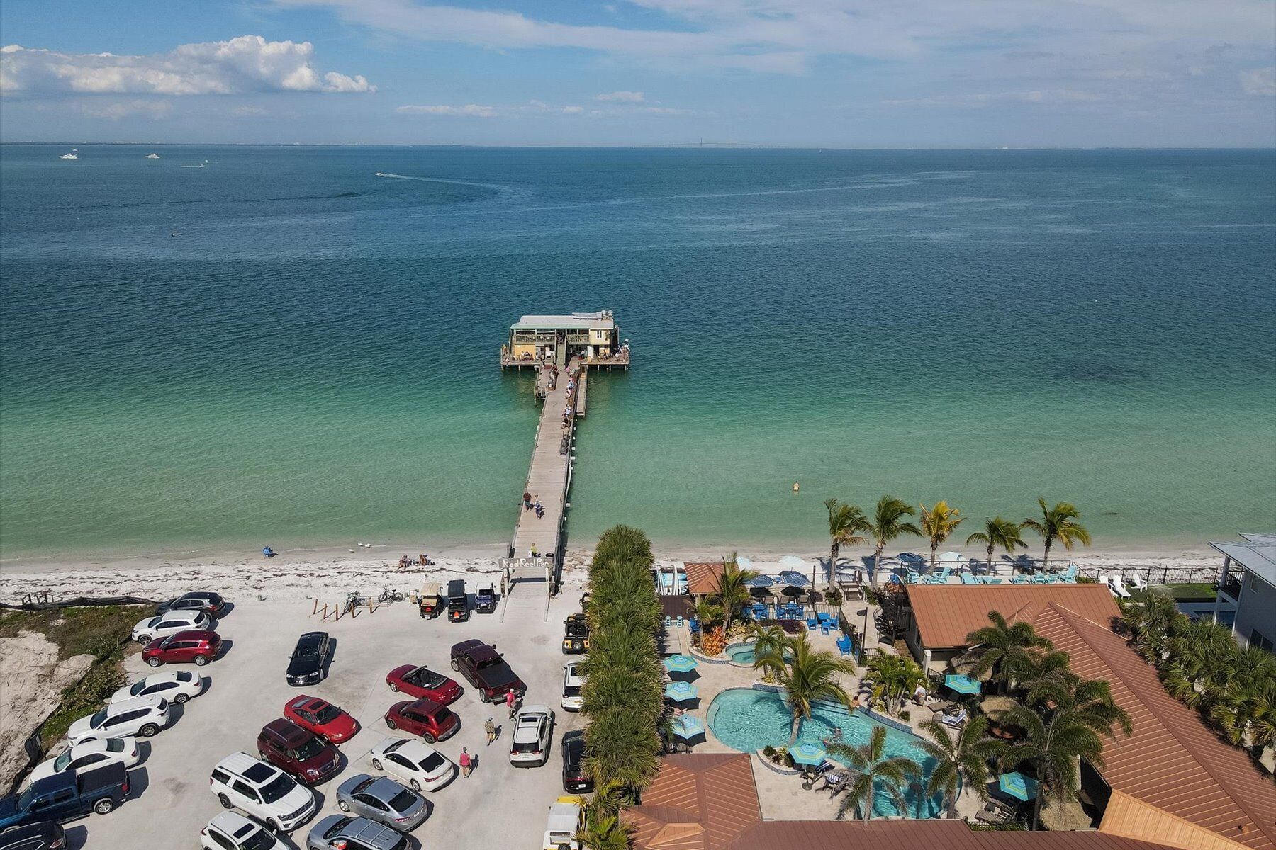 Ein Resort mit einer Anlegestelle, die sich ins Meer erstreckt, einem Parkplatz und einem Poolbereich mit Sonnenschirmen.