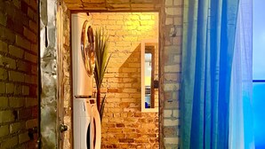 Un espacio interior con pared de ladrillo, una lavadora y una puerta que da a otra habitación.