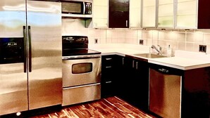 Una cocina moderna con electrodomésticos de acero inoxidable, armarios negros y piso de madera.