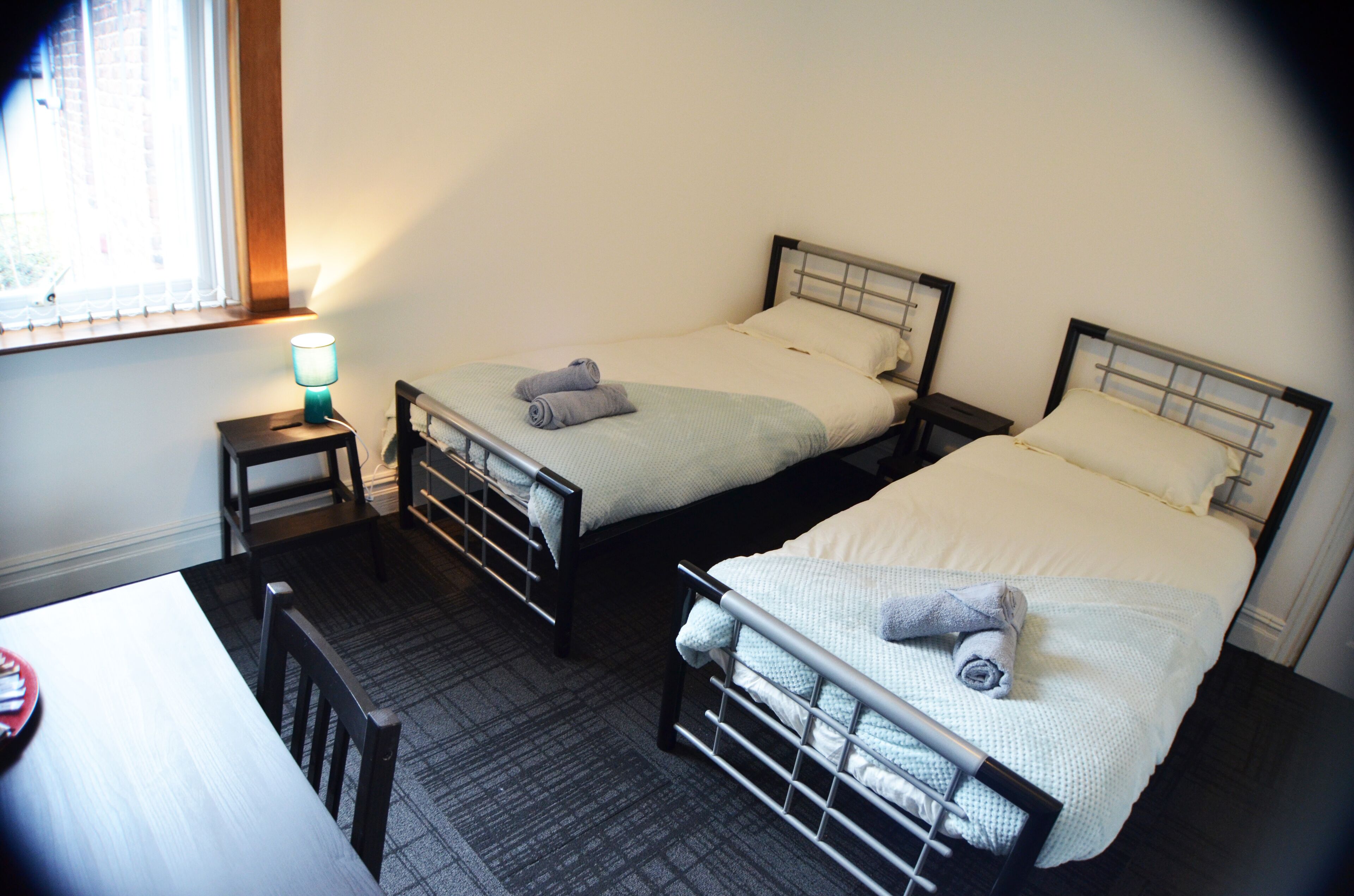 A room with two beds, a small table, and a lamp.