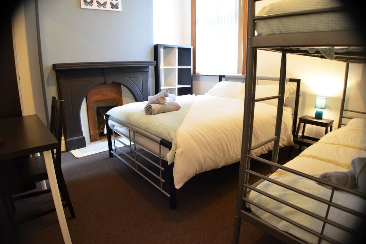 A bunk bed room with a fireplace, a desk, and a nightstand with a lamp.