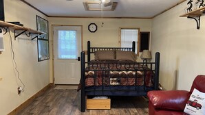 Ein Schlafzimmer mit einem Bett, einem roten Ledersofa, einem Deckenventilator, Holzboden und einer Tür mit Jalousien.
