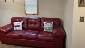 Eine rote Ledersofa mit zwei Kissen, ein Holzregal mit Fahrrädern, ein Fenster mit Jalousien und ein an der Wand befestigter Schädel.