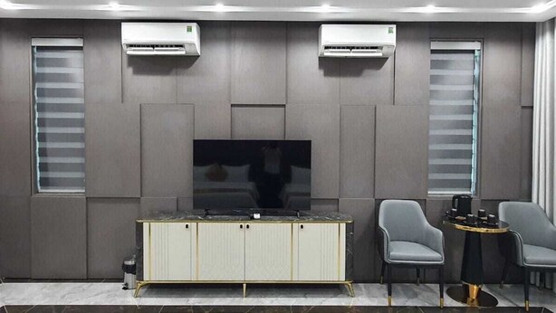 A modern living room with a flat-screen TV, grey chairs, a small round table, and built-in air conditioning units. - palermohotel  (Hanoi)