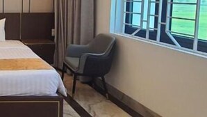 A hotel room with a large bed, a nightstand, a chair, and a window with curtains. - palermohotel  (Hanoi)
