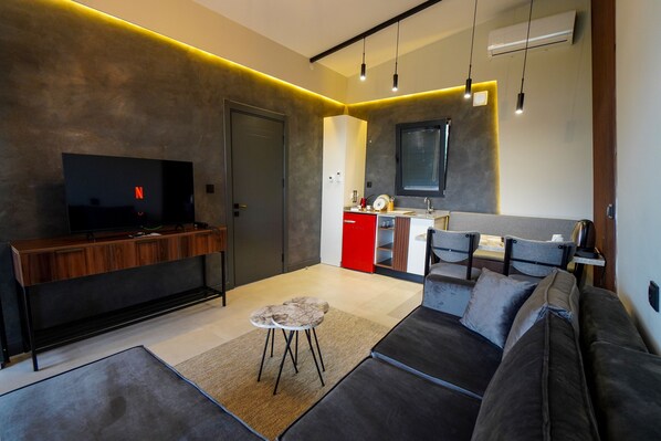 A modern living room with a sofa, a coffee table, and a TV. There is a kitchen area with a red cabinet and a window. - Lake Look Sapanca (Sapanca)