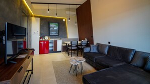 A modern living room with a black leather sofa, a wooden coffee table, and a TV on a wooden stand. There is a kitchen area with a red fridge and a dining table with chairs. - Lake Look Sapanca (Sapanca)
