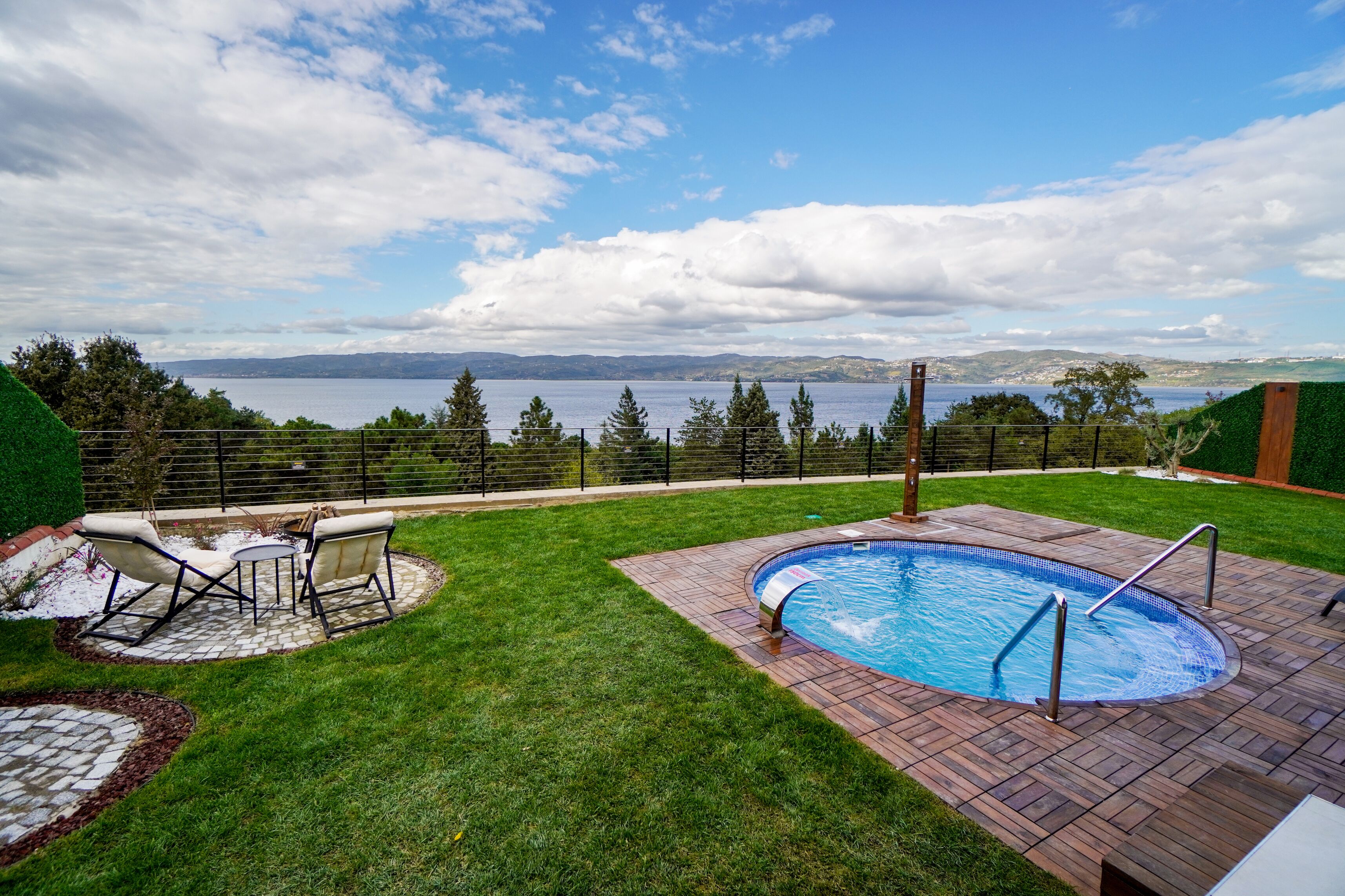 A backyard with a swimming pool, a patio with outdoor furniture, and a view of a lake and mountains.