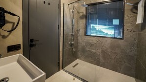 Et moderne badeværelse med brusebad i hele bredden, en føntørrer på væggen og et vindue med udsigt over bybilledet.