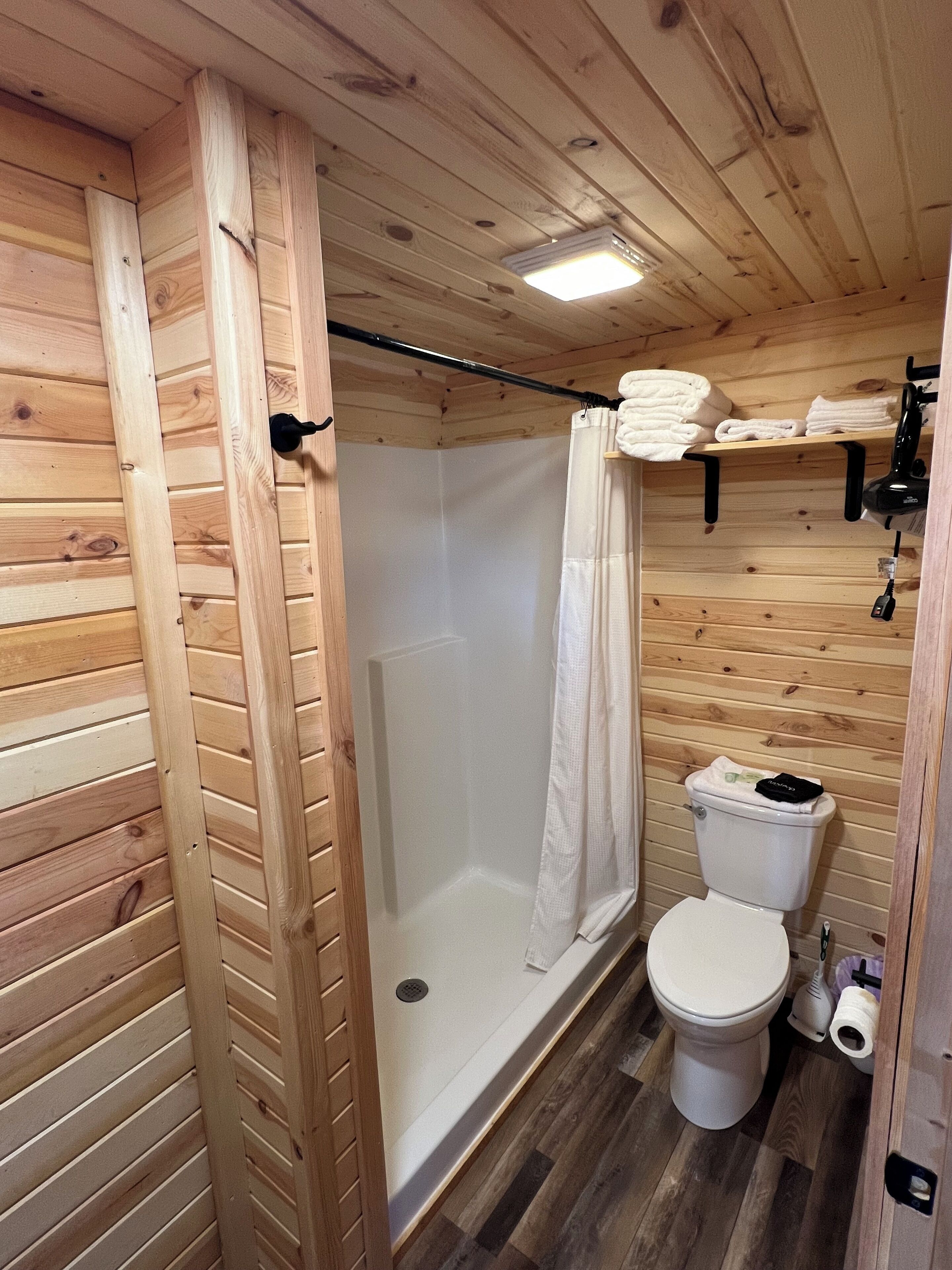 Een betegelde badkamer met een douche, toilet en planken met handdoeken.