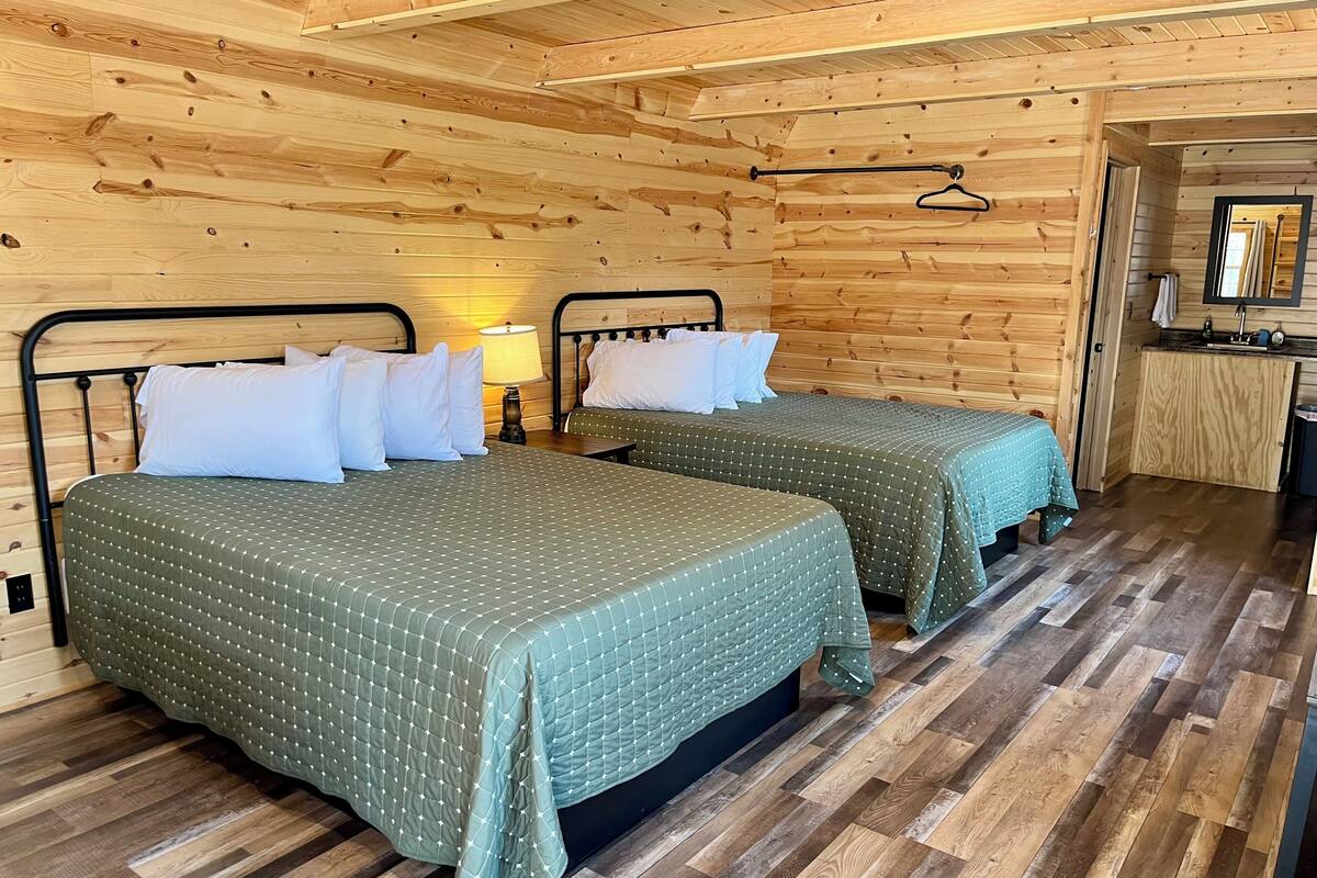 A wooden cabin room with two beds, a small table, and a mirror.