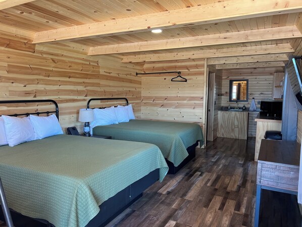 A wooden cabin with two beds, a small kitchenette, and a mirror.