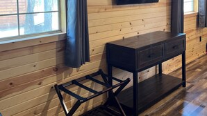 Una habitación con paneles de madera, un televisor montado en la pared, una mesita y una ventana con cortinas.