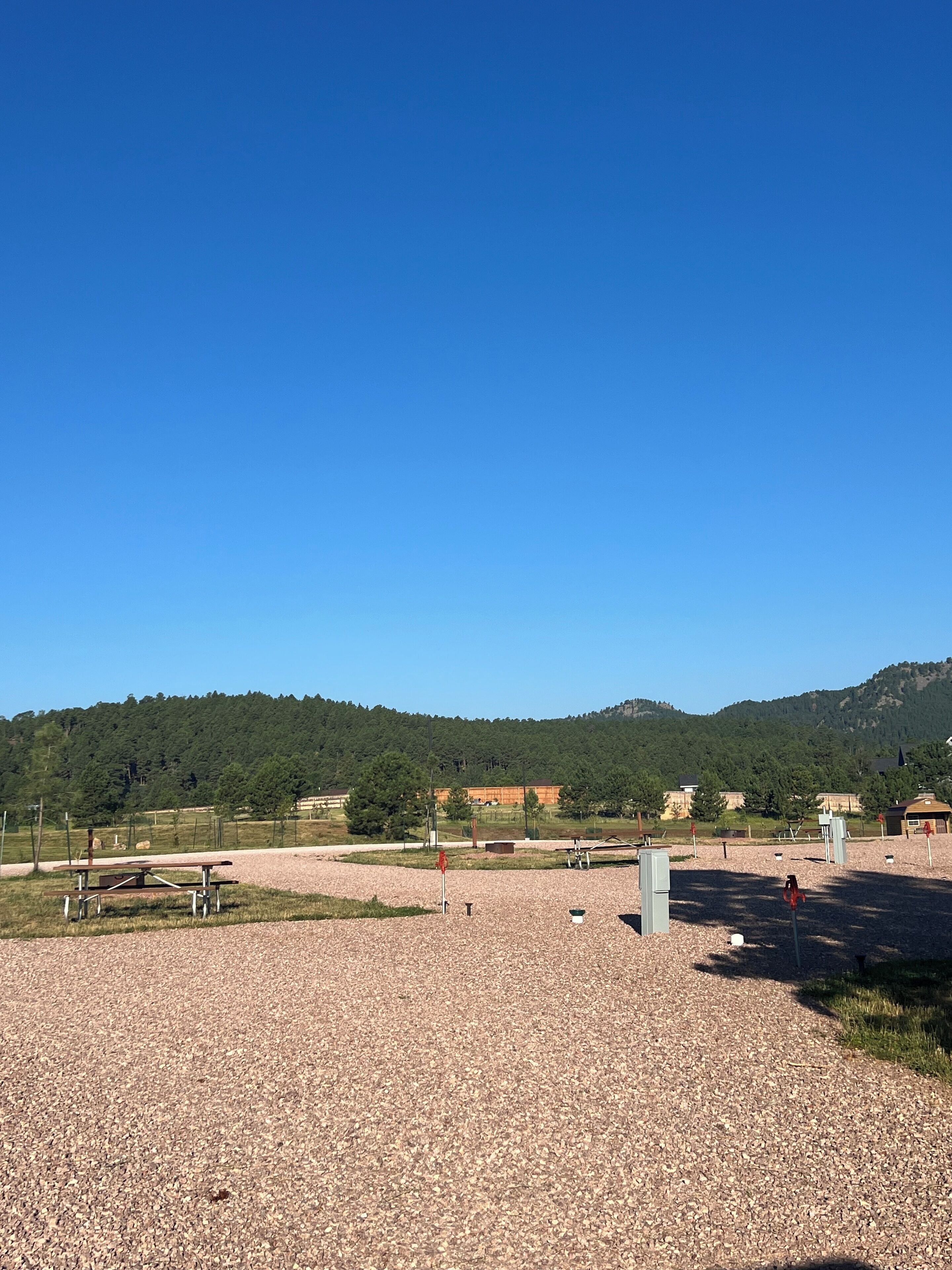 A gravel area with a picnic table, utility boxes, and a clear view of a forested hill in the background.