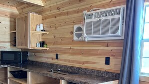 Cocina con armarios de madera, microondas, aire acondicionado integrado y un cesto de basura.