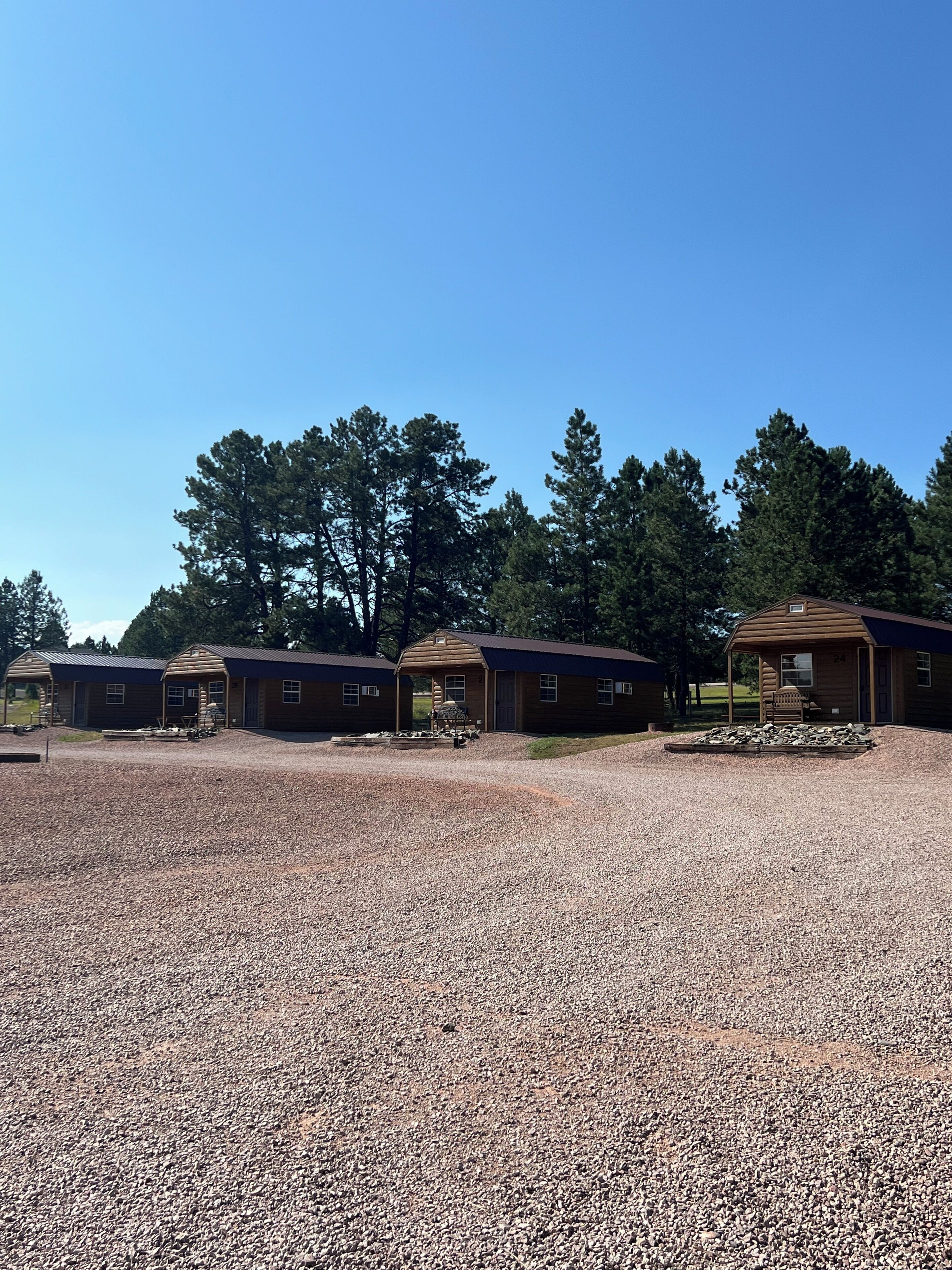 Une rangée de chalets en bois, avec des allées recouvertes de gravier, entourés d’arbres.