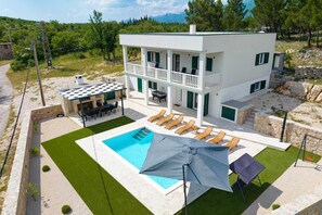 Una casa moderna de dos pisos con balcón, piscina y mobiliario para exteriores.