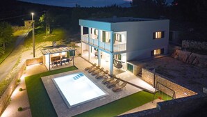 Edifici modern de dues plantes amb piscina, zona d'estar a l'aire lliure i mur de contenció de pedra.