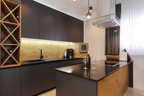 Eine moderne Küche mit dunklen Schränken, einer Holz-Spritzschutzwand und einer zentralen Kochinsel mit Weingläsern.