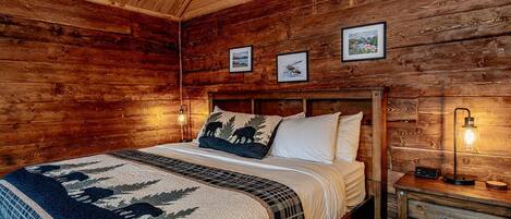 A wooden cabin bedroom with a bed, a nightstand, and framed pictures on the wall.