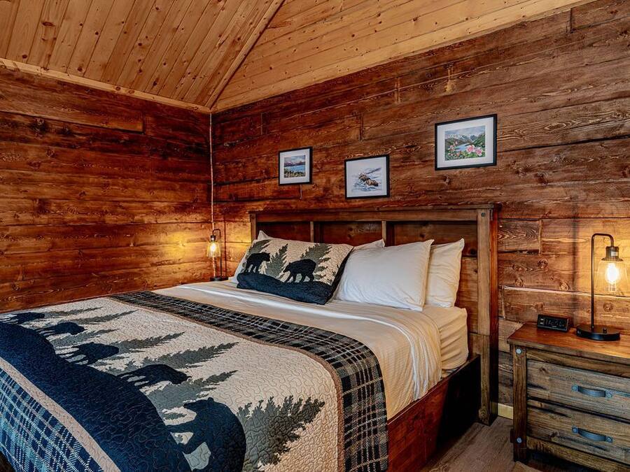 Une chambre dans un chalet en bois, avec un lit, une table de chevet et des tableaux encadrés accrochés au mur.