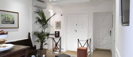A modern hotel lobby with a wooden reception desk, a potted plant, a framed picture, and a closed door.