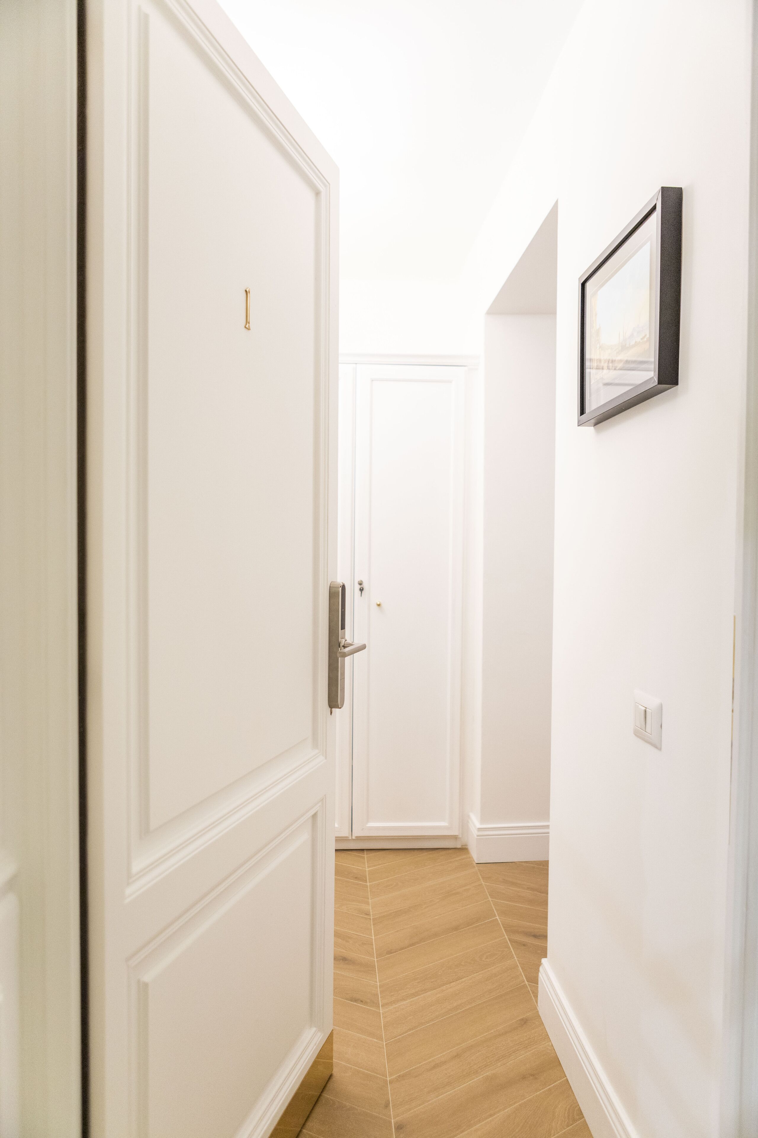 Un passadís amb una porta blanca, un quadre al mur i un paviment de fusta.