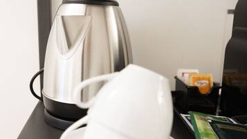 A table with a stainless steel kettle, a white cup, a plate, a spoon, and a packet of tea.