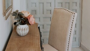 A hallway with a double door, a wooden bench, a white vase with flowers, and a mirror on the wall.