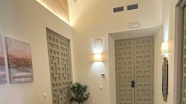 A room with a yellow sofa, a small round table, a lamp, and a wall-mounted light fixture.