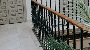 A staircase with a wooden handrail and black balusters, leading to a door with a geometric pattern.