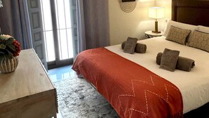 A hotel room with a bed, a bedside table with a vase, a lamp, and a view of the outside through a window with curtains.