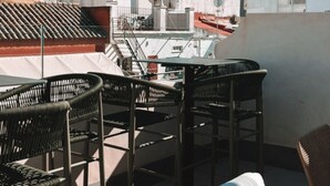 A rooftop terrace with wicker furniture, a striped sofa, and a view of a historic tower.