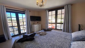 A hotel room with a large bed, a flat-screen TV, a dresser, and a balcony with a view of the city. - Apt. Brisa Marina  (Valle Gran Rey)