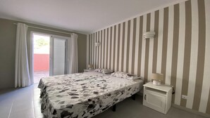 Et soveværelse med en seng, et natbord, en lampe og et vindue med gardiner.