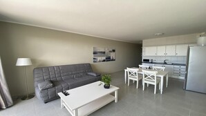 En moderne lejlighed med en grå sofa, et hvidt sofabord, et spiseområde med hvide stole, et køkken med hvide skabe og en grå gulv.