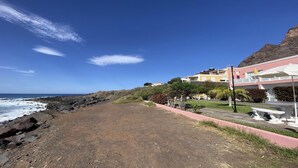 En ejendom ved kysten med en stenstrand, klar himmel og en bygning med altaner.