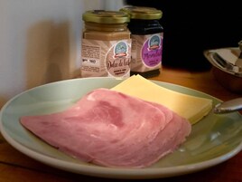 Un plato con jamón, queso y un frasco de dulce de leche.