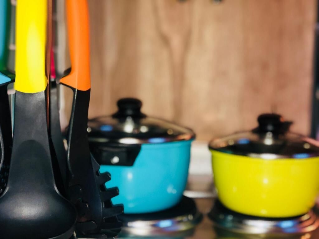 Close-up de utensílios de cozinha e panelas coloridas sobre um fogão.