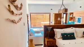 Un dormitorio con cama, mesitas de noche, una mesita auxiliar de madera, un florero y una ventana con persianas.