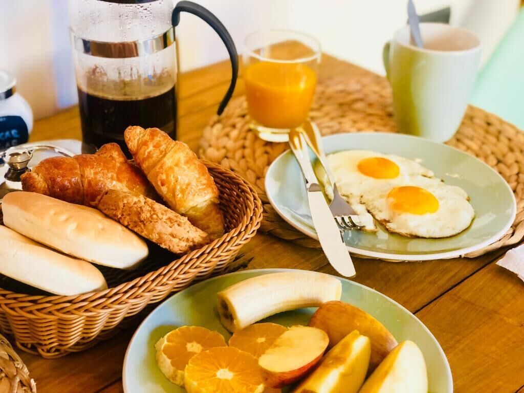 A breakfast setting with croissants, eggs, bananas, and oranges on a table.