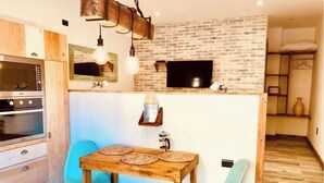 Una cocina funcional con una mesa de madera, dos sillas, un televisor fijado en una pared de ladrillo y un microondas.